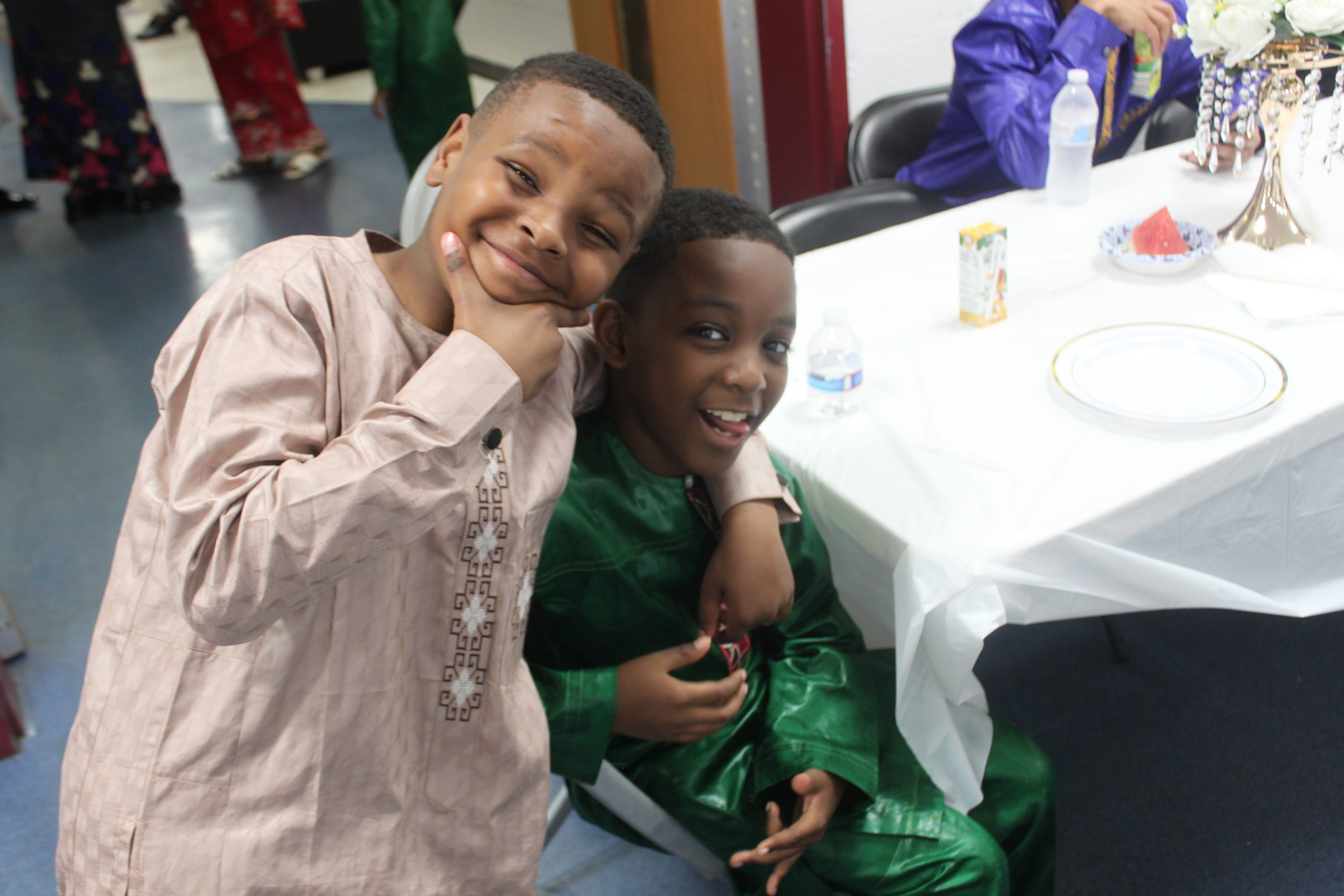 Two smiling young boys in traditional attire embracing at a Fulani community dinner