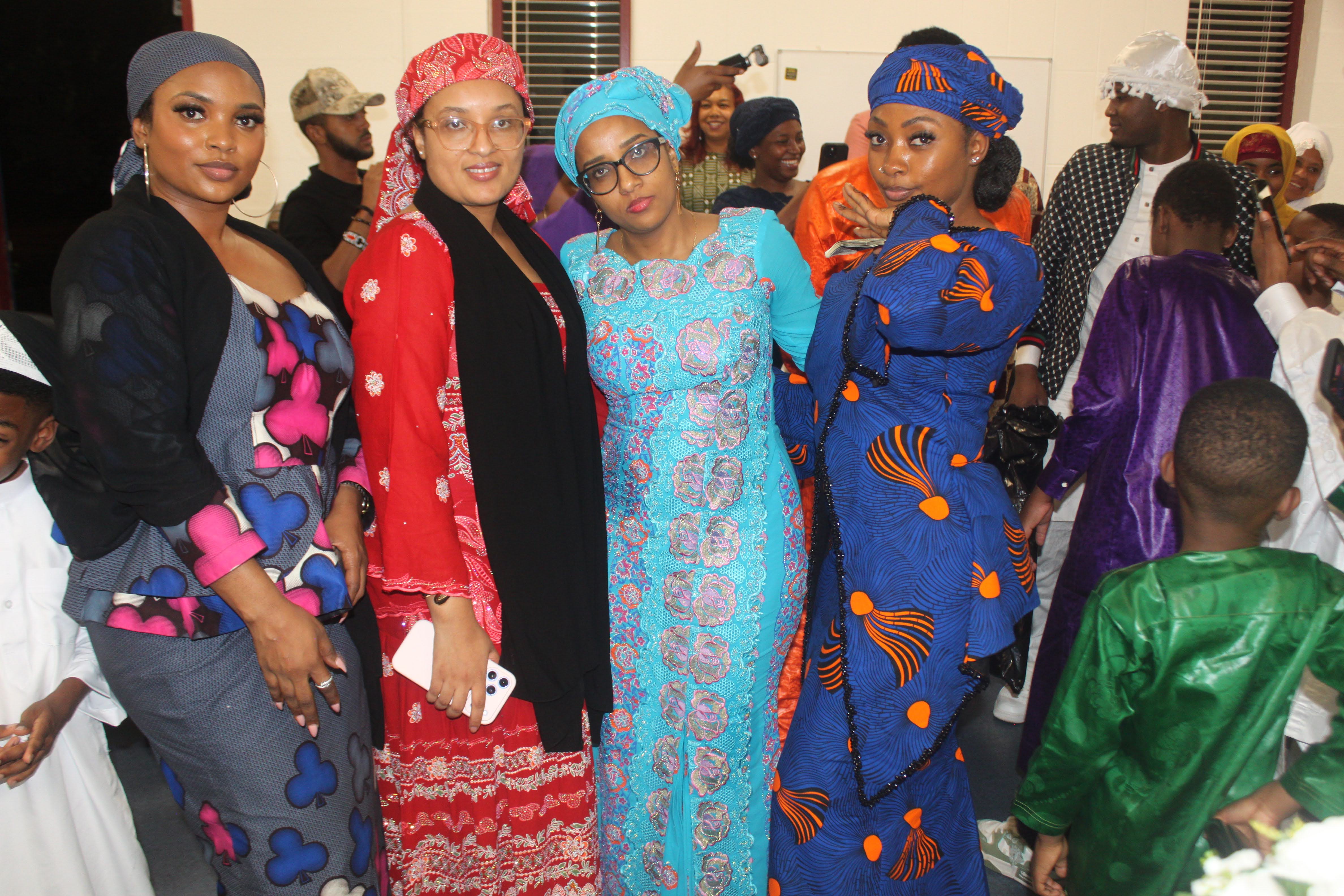 Four Fulani women in vibrant traditional dresses and headwraps smiling together at the Al Ada community dinner